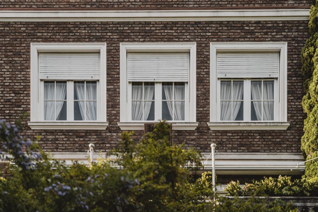 Drei Fenster mit halbgeschlossenen Rollläden an einer Backsteinfassade.