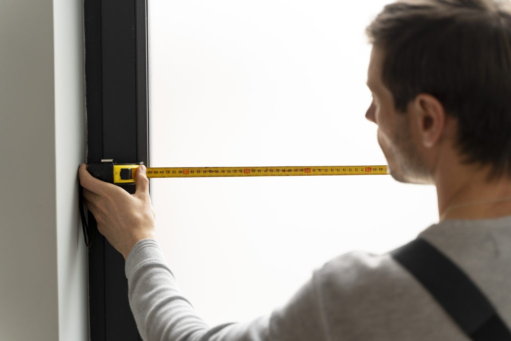 Handwerker misst Fensterbreite mit einem Maßband.