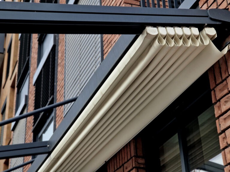 Eine rollbare Pergola mit plissierter Plane ist an der Hauswand befestigt.